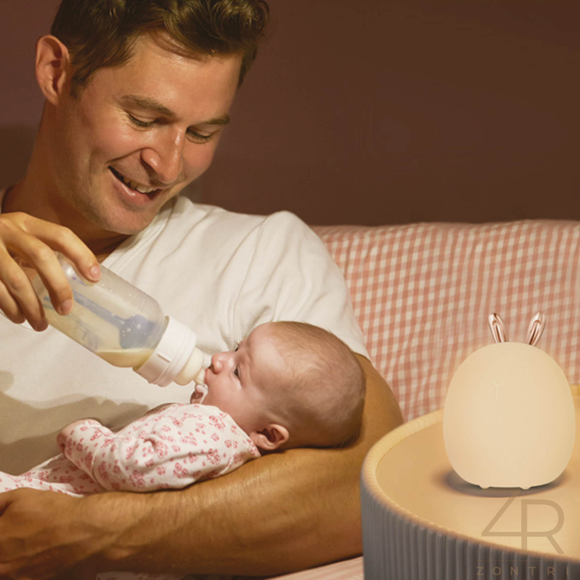  Father feeding a newborn baby from a bottle while a warm-glow rabbit night light sits on the bedside table.