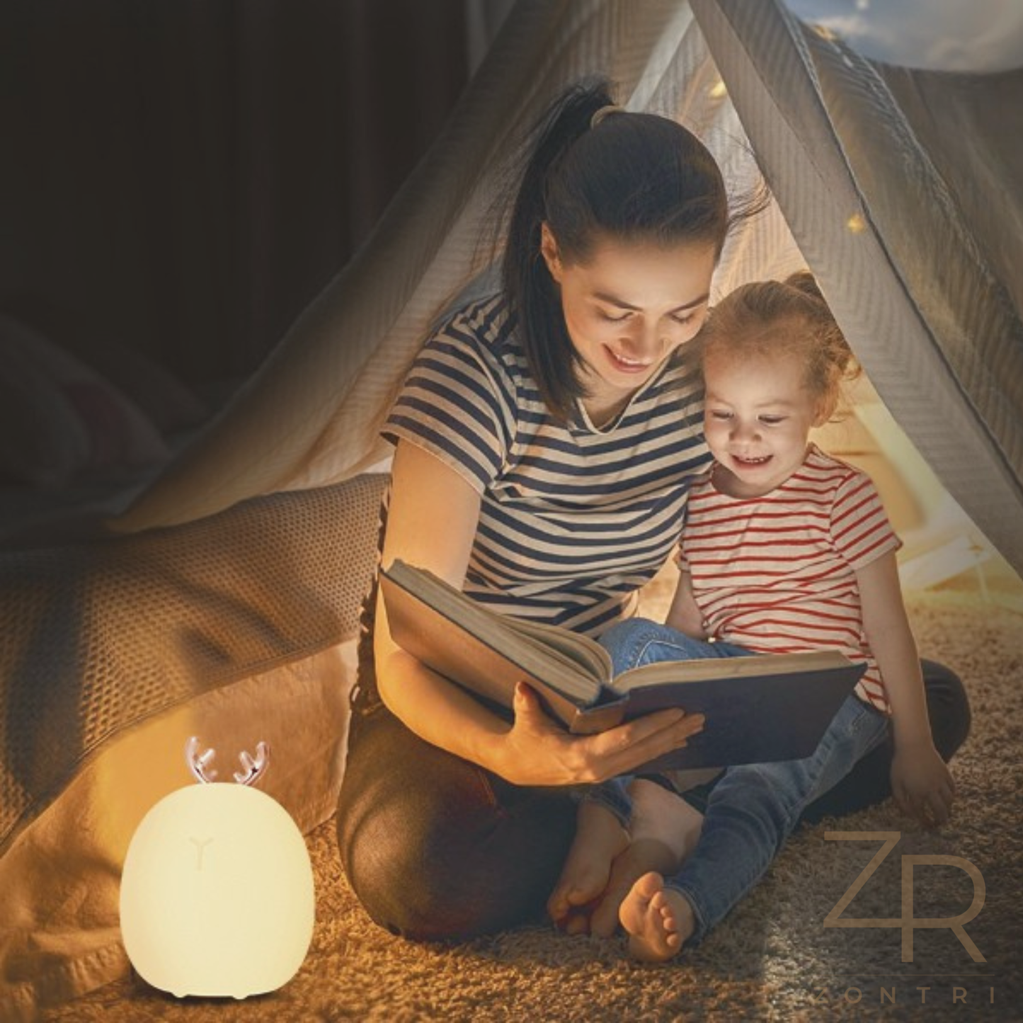 Mom and daughter reading a book inside a tent with a glowing silicone deer night light on the floor.