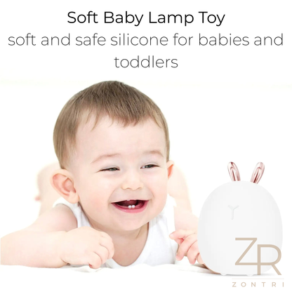 Smiling baby lying on a white background next to a soft silicone bunny (rabbit) night light branded by ZONTRI.